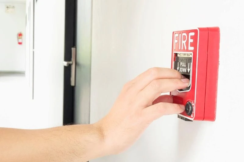 Mão de pessoa acionando botão de alarme de incêndio na parede.