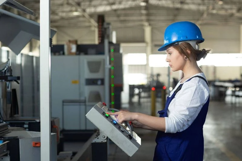 Sistema SCADA: como funciona e benefícios para a indústria Mulher usando capacete azul e operando um painel de controle em uma indústria.