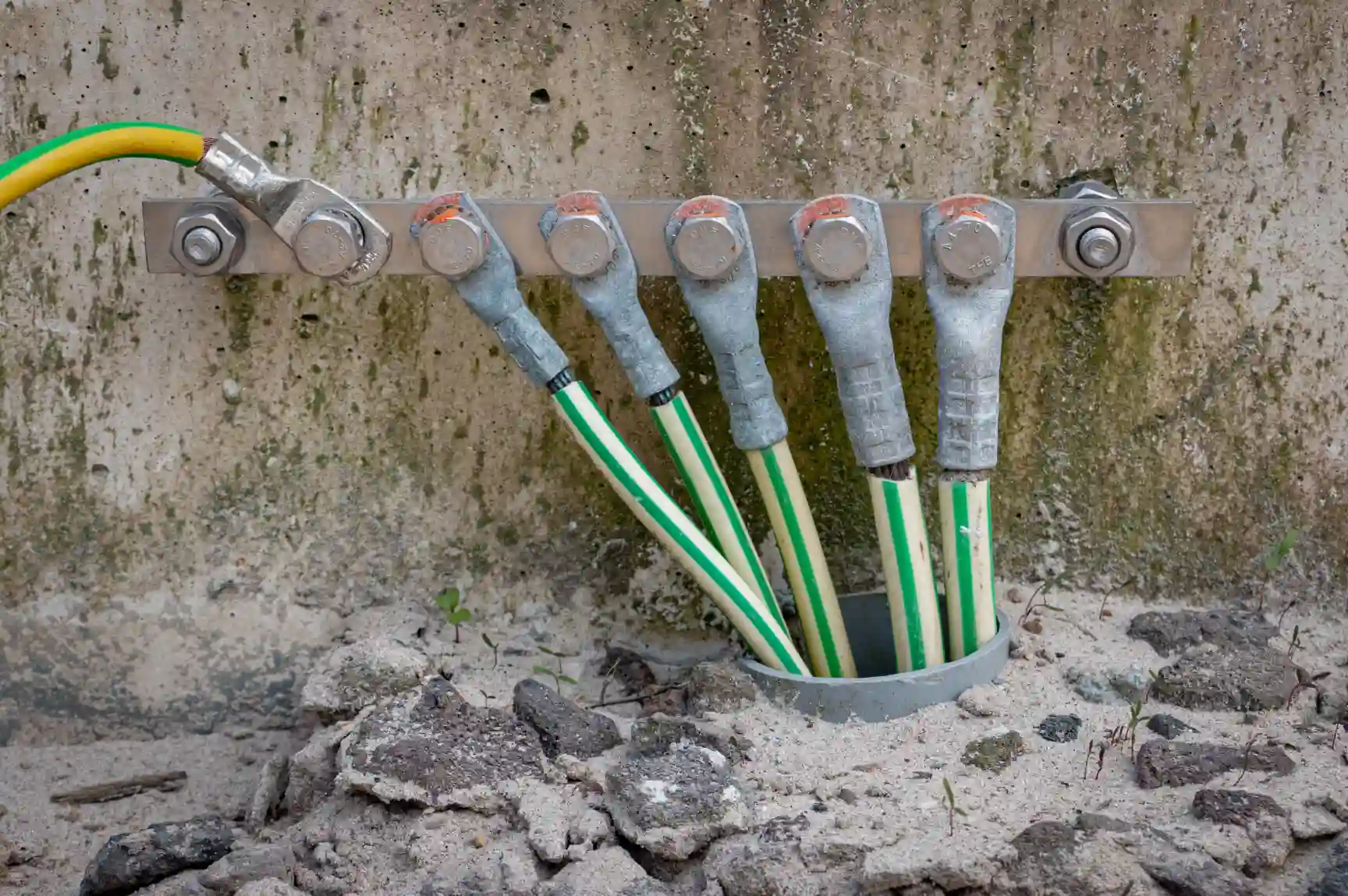 Imagem mostrando um sistema de aterramento com cabos conectados a uma haste de aterramento instalada na parede de concreto, essencial para segurança elétrica.