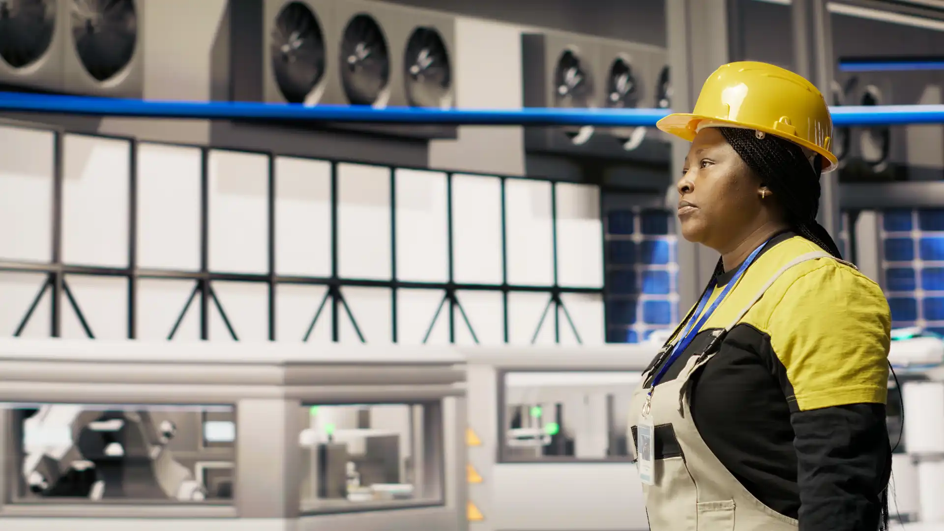 Mulher engenheira vestida com capacete de segurança amarelo observando equipamentos industriais em uma fábrica de tecnologia.